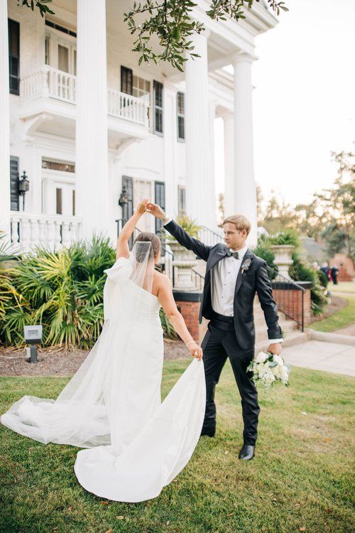 A bride and groom are dancing in front of a large white building.