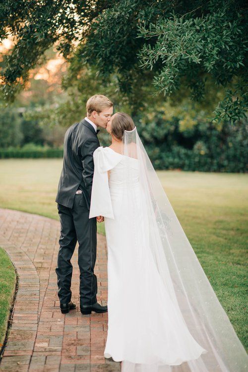 A bride and groom are kissing on a brick walkway.