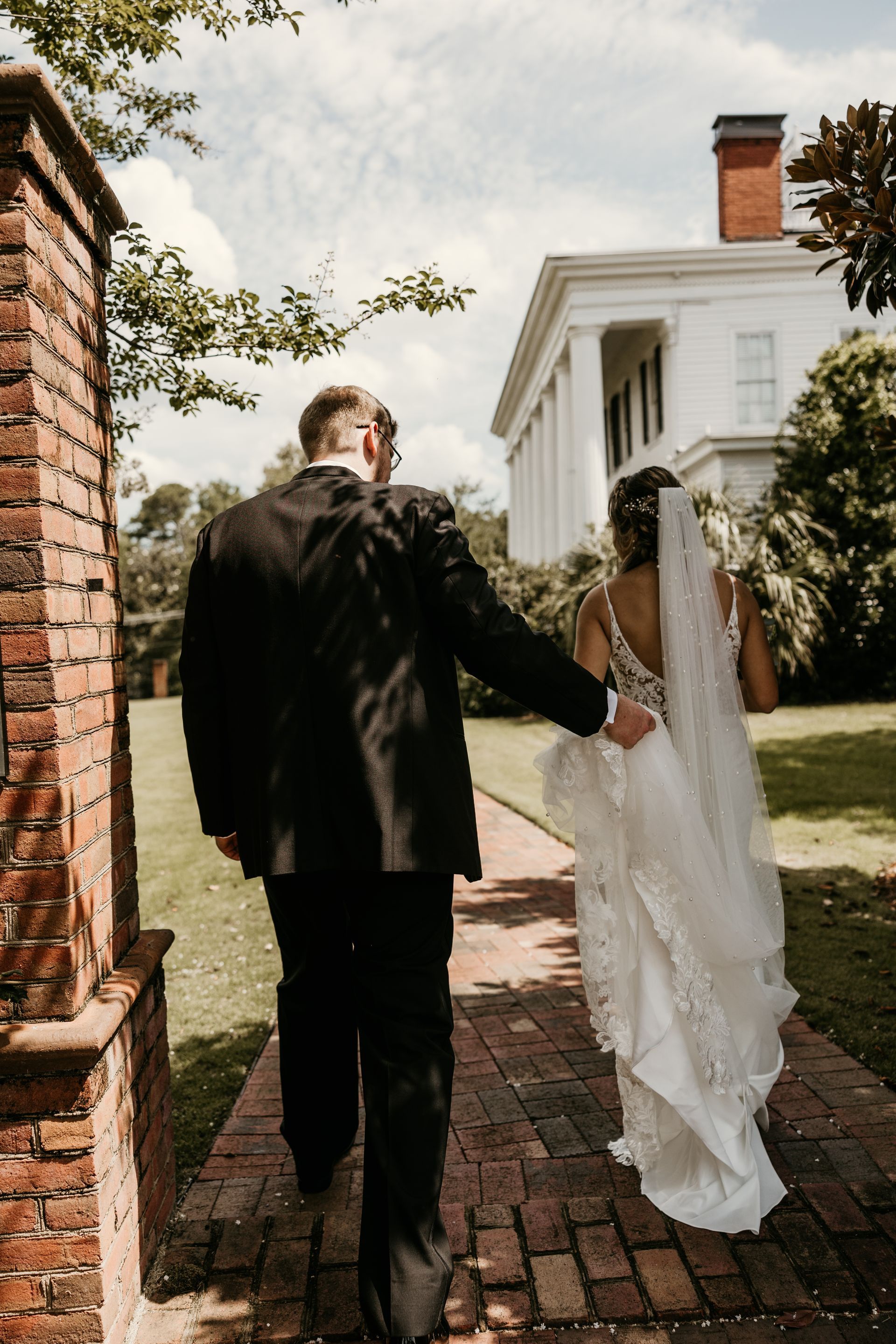 A bride and groom are walking down a sidewalk in front of a large white building.