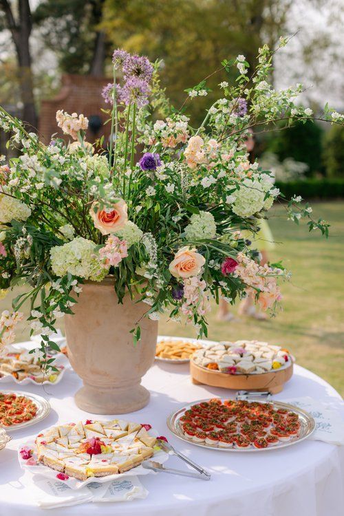 A table with a vase of flowers and plates of food on it.