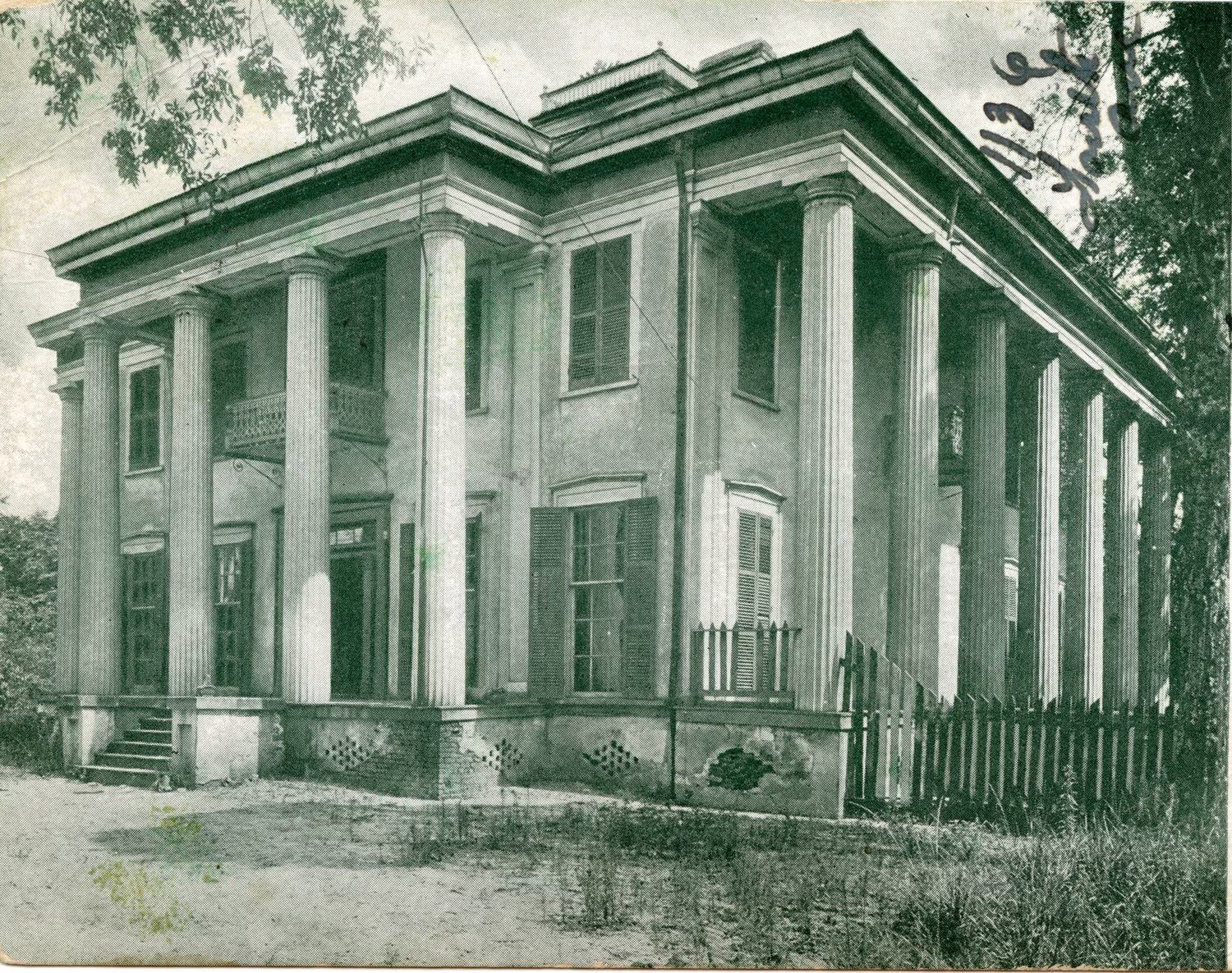 A black and white photo of a large house with columns