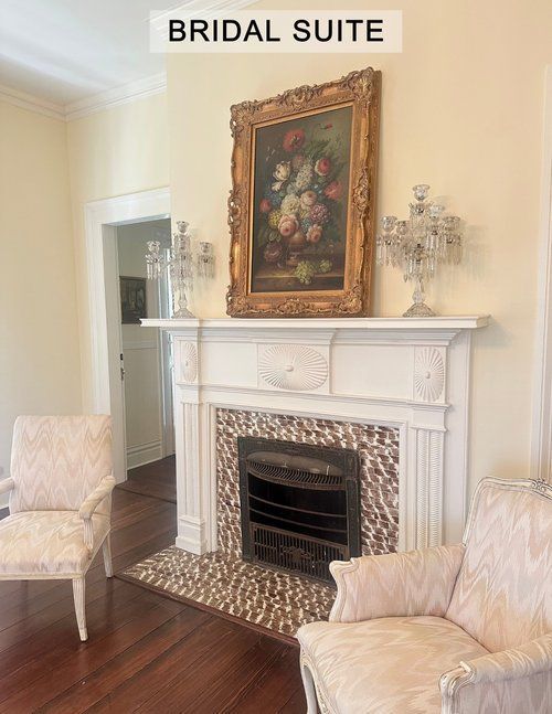A living room with a fireplace , chairs and a painting on the wall.