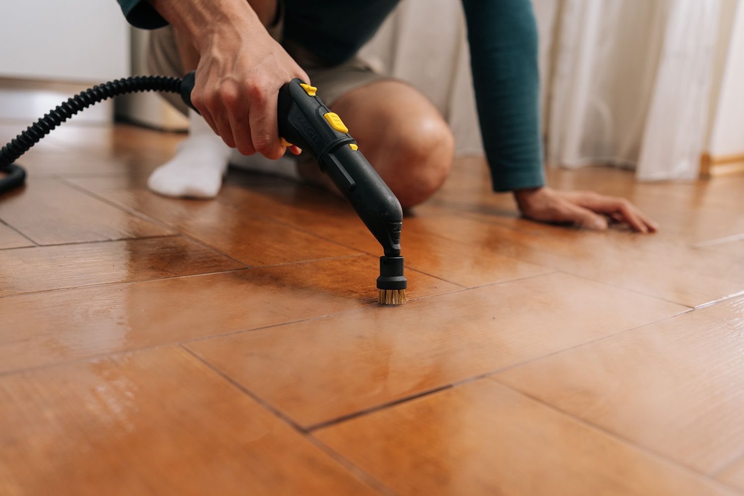 Person steam-cleaning a hardwood floor with a black handheld cleaner