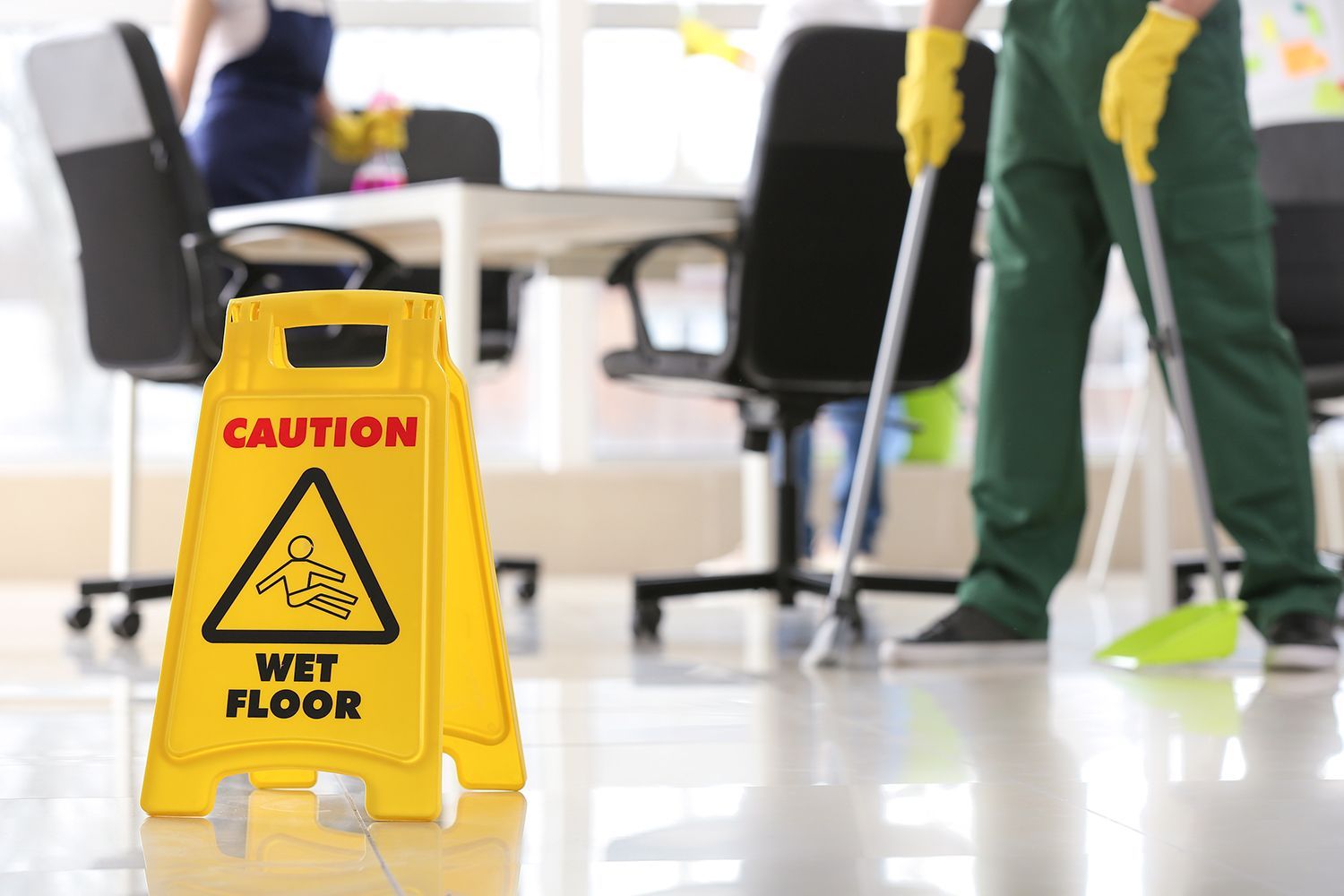 Yellow caution wet floor sign in an office while a cleaner mops the floor