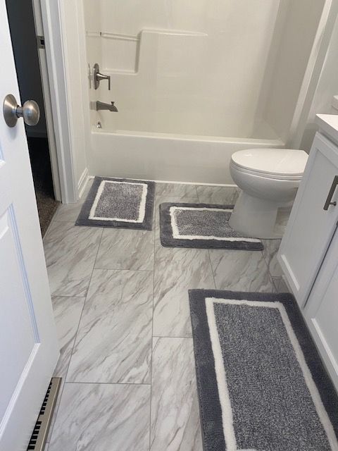 Small bathroom with shower, toilet, and gray bath mats on a marble-pattern floor. Small bathroom with shower, toilet, and gray bath mats on a marble-pattern floor.