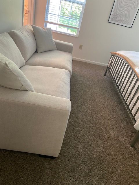 Small bedroom with a white couch, window, and bed on beige carpet.