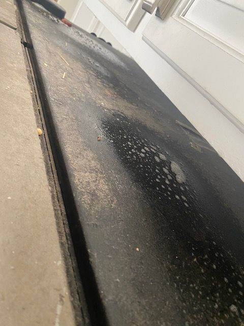 Wet black asphalt driveway beside a white garage wall with scattered debris