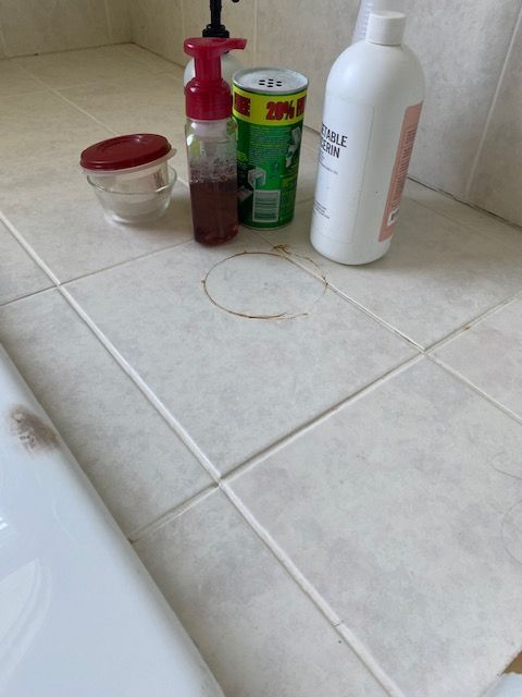 Bathroom counter with lotion, jar, red pump bottle, green can, and white bottle on tiled floor