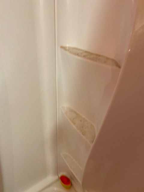 Close-up of a beige tiled corner with peeling patches and a small red-and-yellow object at the bottom.