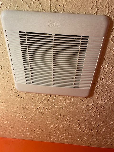 White ceiling vent with slatted grille on a textured peach ceiling at an angle