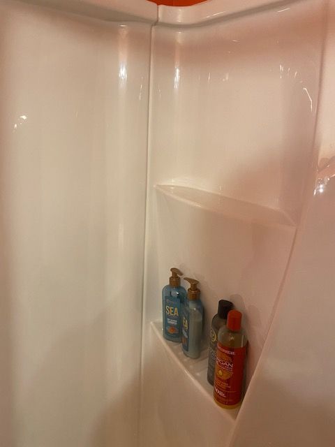 Shower stall corner with built-in shelf holding bottles of shampoo and body wash