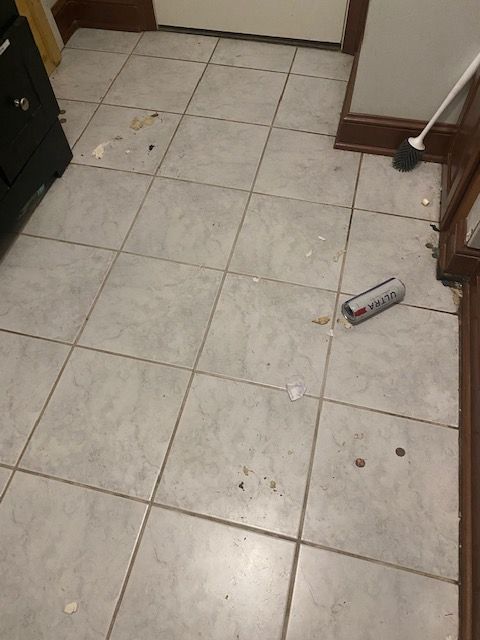 Kitchen floor with scattered debris and a tipped-over can near the cabinets