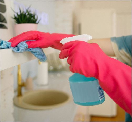 Person in pink gloves cleaning a bathroom sink with a spray bottle and cloth
