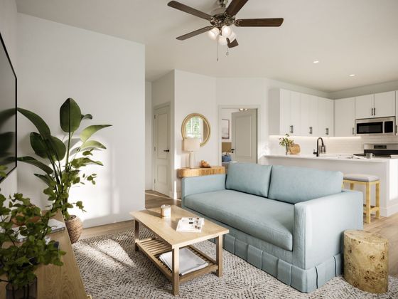 Bright living room with a blue sofa, coffee table, houseplant, and open kitchen in the background