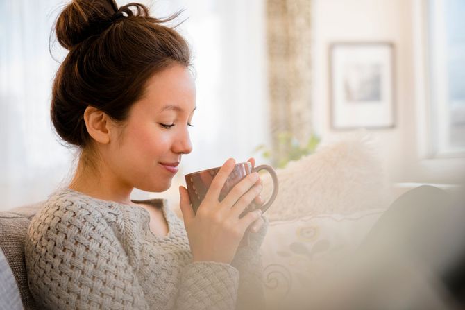 Woman in a cozy sweater holding a mug and smiling by a bright window