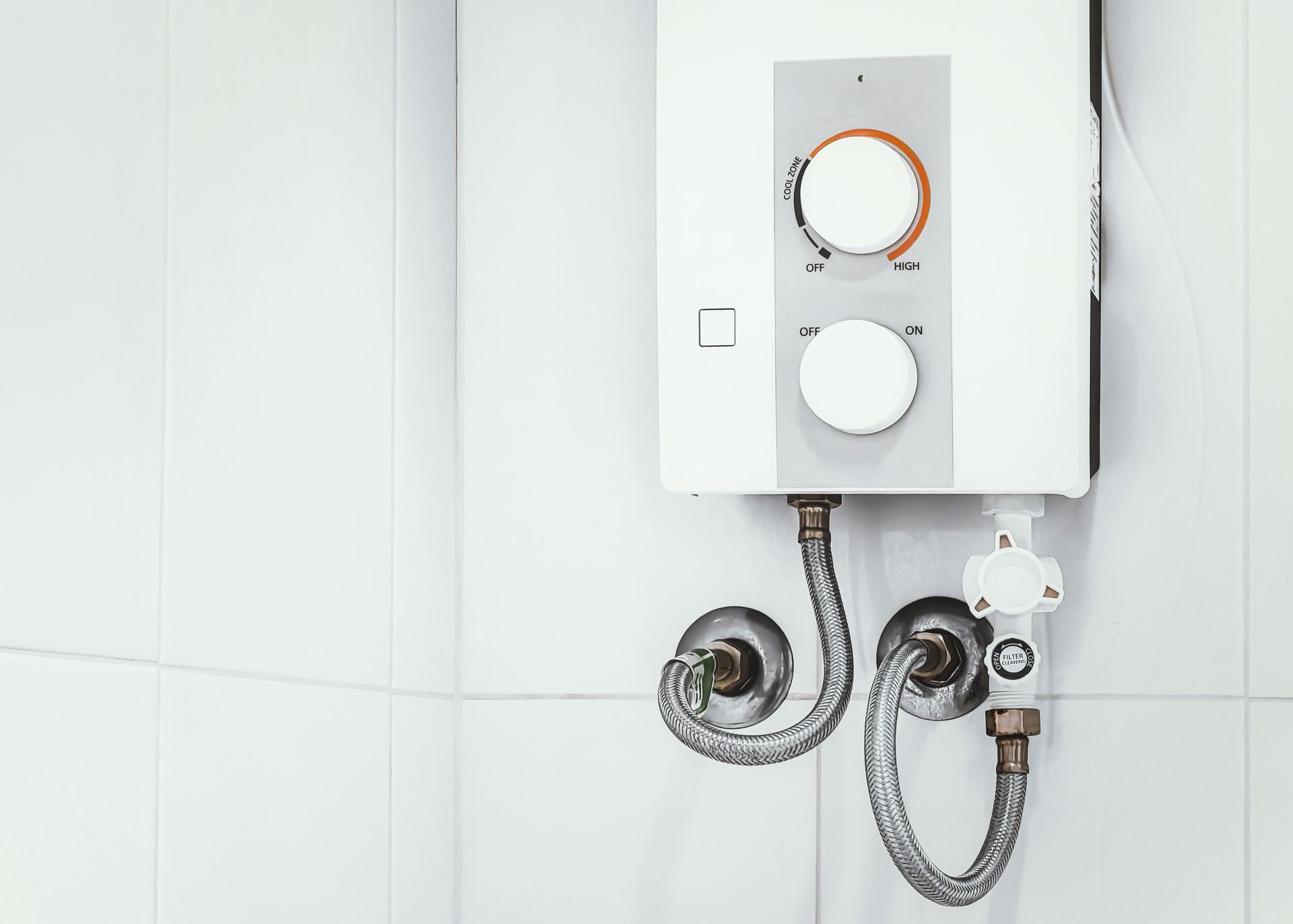 Wall-mounted white water heater with two shower hoses and knobs in a tiled bathroom
