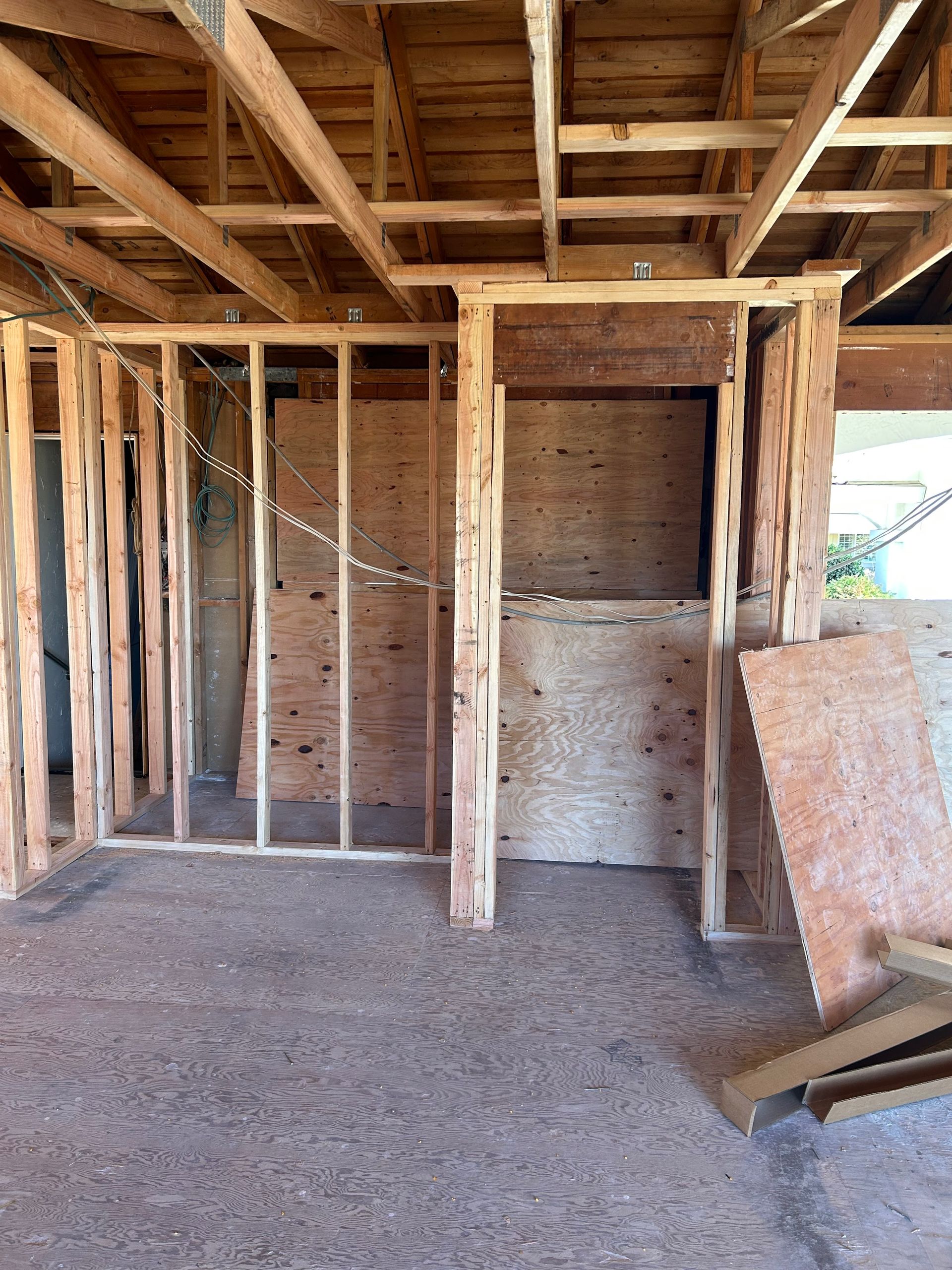 Interior view of a residential construction site featuring exposed wood wall framing and a partial plywood partition wall.