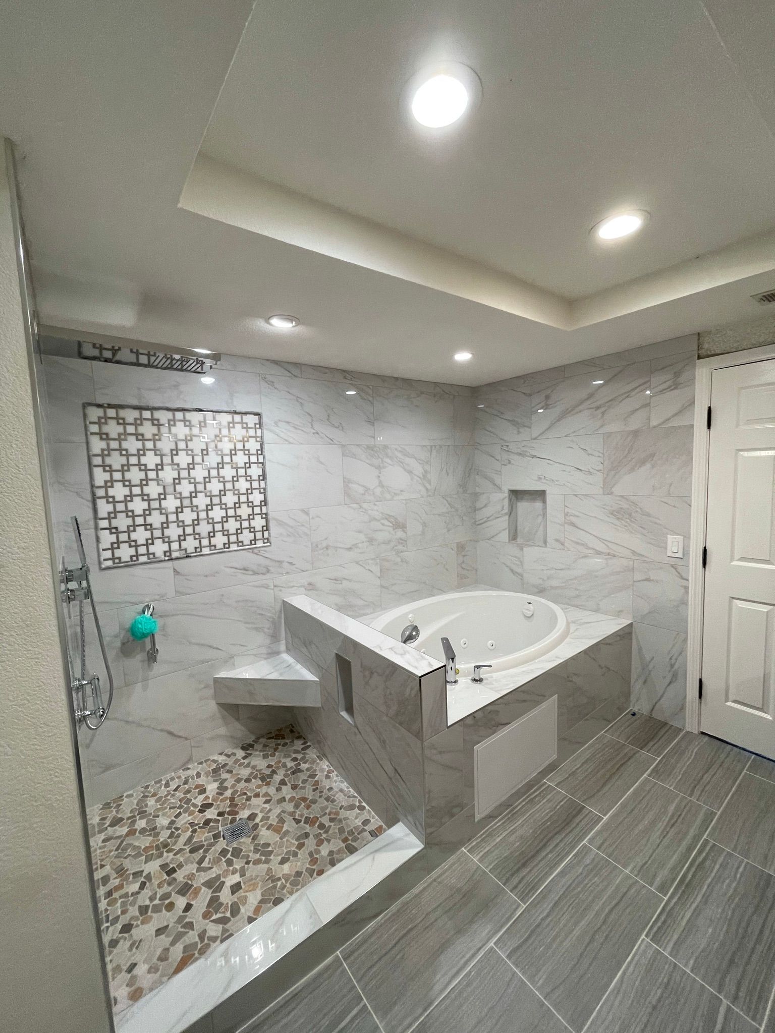 A modern bathroom featuring a walk-in shower with a pebble floor, a corner soaking tub, and gray tile throughout.