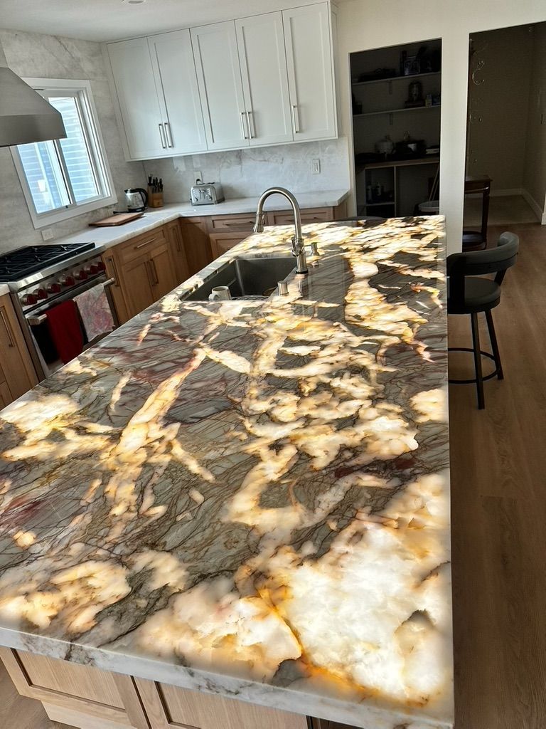A kitchen island with a striking, backlit, dark-patterned stone countertop sits in a kitchen with light wood cabinetry.