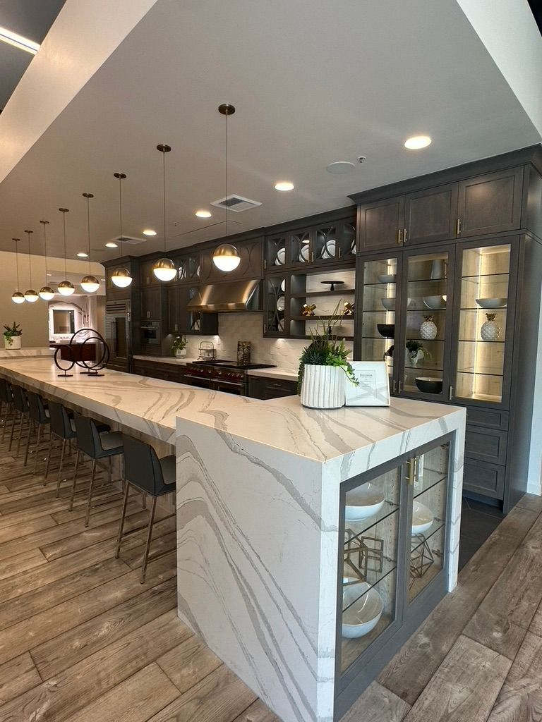 A long, modern kitchen island with marble-patterned countertops and bar seating in a room with dark wood cabinetry.