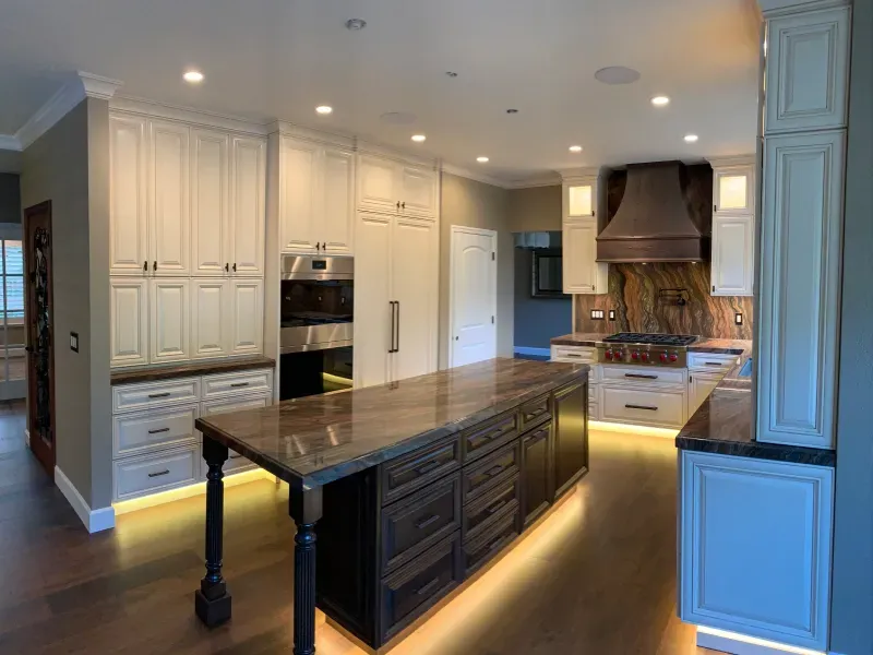 A modern kitchen with white cabinetry, a dark brown island, marble countertops, and under-cabinet LED lighting.
