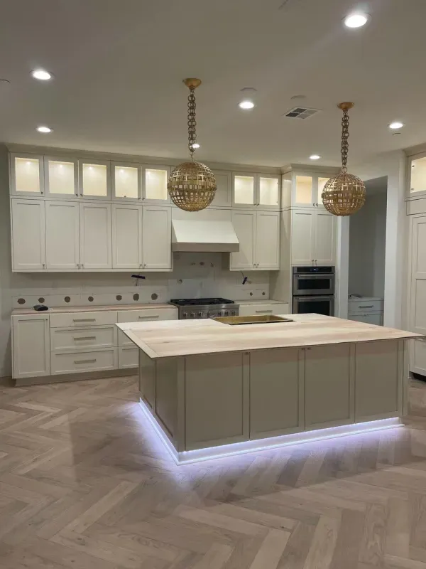 Modern kitchen featuring white cabinets, a central island with wood countertop and under-cabinet lighting, and wood floors.
