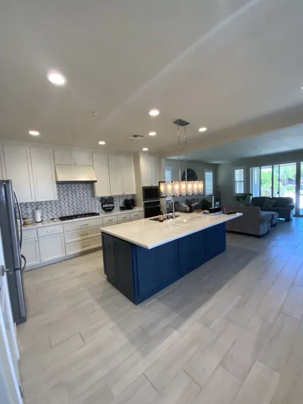 A modern kitchen with white cabinetry, a large navy blue island with a stone countertop, and light tile flooring.