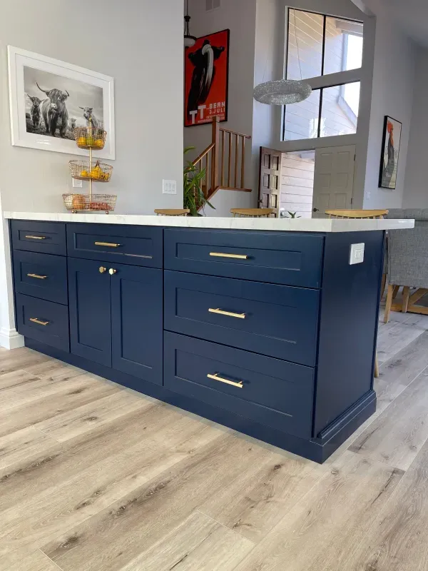 A navy kitchen island with gold hardware and a white countertop sits on light wood-look flooring in a bright room.