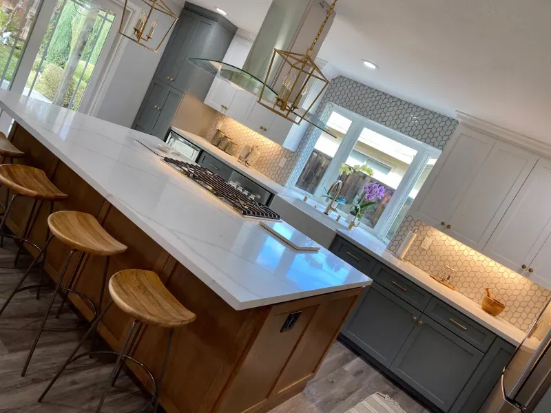 A modern kitchen with a large island featuring a white countertop, three wooden stools, and grey and white cabinets.