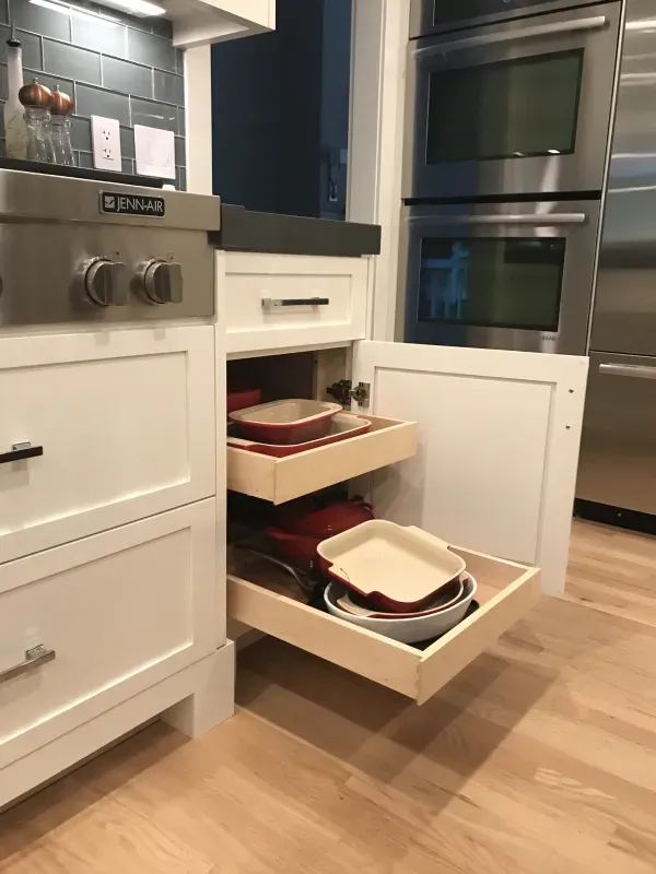 A kitchen cabinet with two pull-out wooden drawers filled with various baking dishes and pans.
