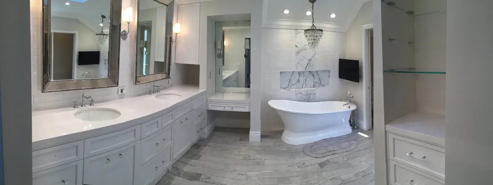A wide-angle shot of a luxurious bathroom with white cabinets, a double vanity, a freestanding tub, and marble flooring.