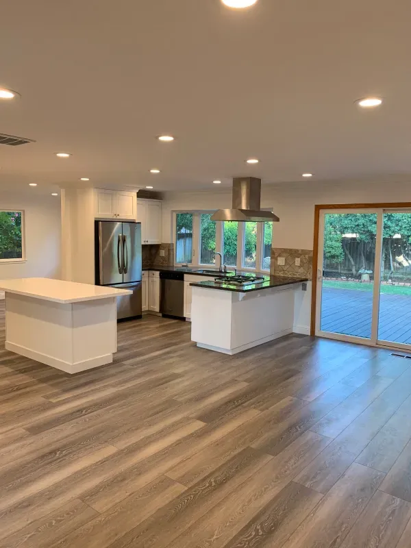 Modern kitchen with white cabinets, dark countertops, wood-look flooring, stainless appliances, and sliding glass doors.
