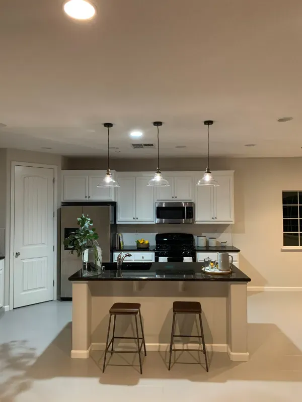 A modern kitchen featuring white cabinets, stainless steel appliances, a black island with two stools, and three pendants.