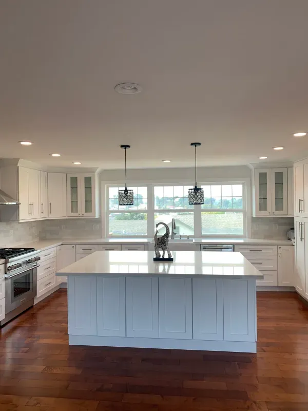A bright kitchen with white cabinets, a large central island, stainless steel appliances, and dark hardwood floors.