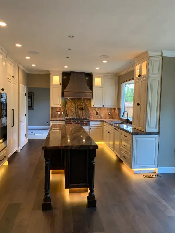 A modern kitchen with white cabinetry, a dark wood island, a stone backsplash, and warm under-cabinet lighting.