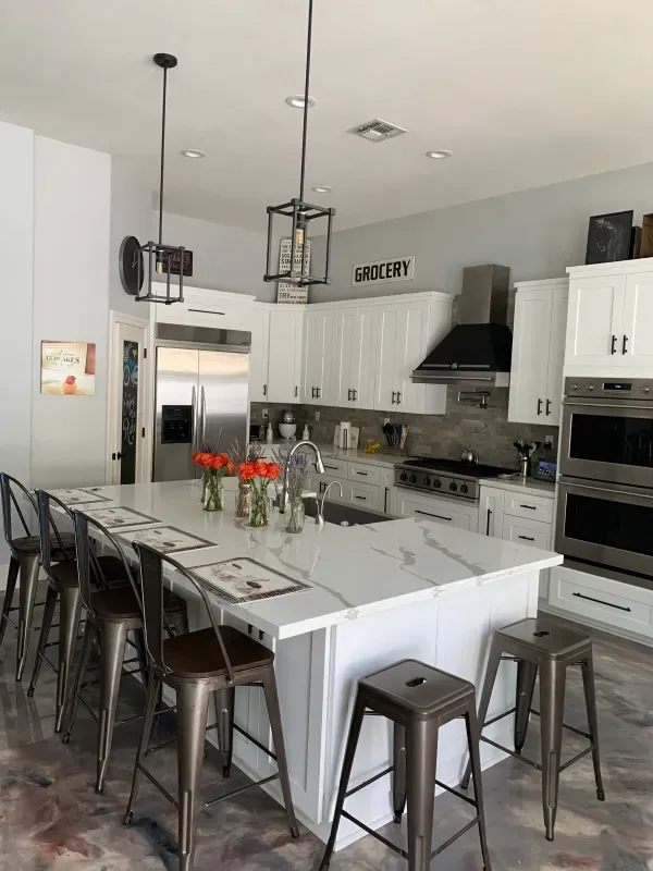 A bright, modern kitchen featuring a marble-topped island with metallic stools, white cabinetry, and stainless appliances.