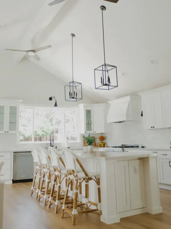 A bright, modern kitchen featuring a white center island with woven bar stools, pendant lighting, and a vaulted ceiling.