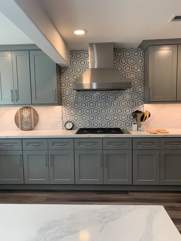 A modern kitchen featuring gray shaker cabinets, white countertops, and a patterned hexagonal tile backsplash.
