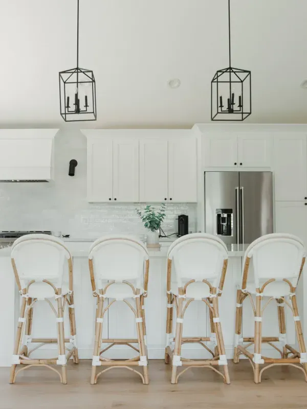 A bright kitchen island with four white and rattan bar stools under two modern black metal lantern pendant lights.