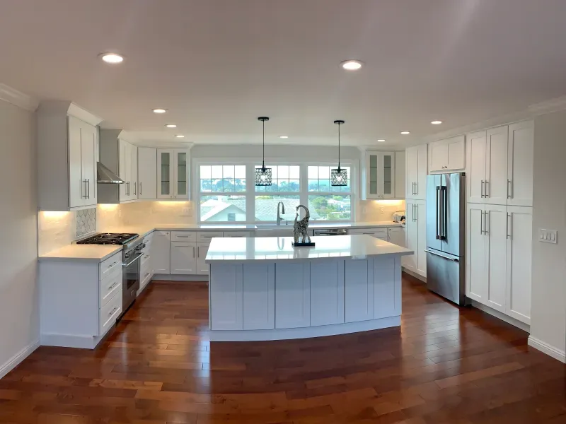 A modern kitchen with white cabinets, a large central island, stainless steel appliances, and dark hardwood floors.