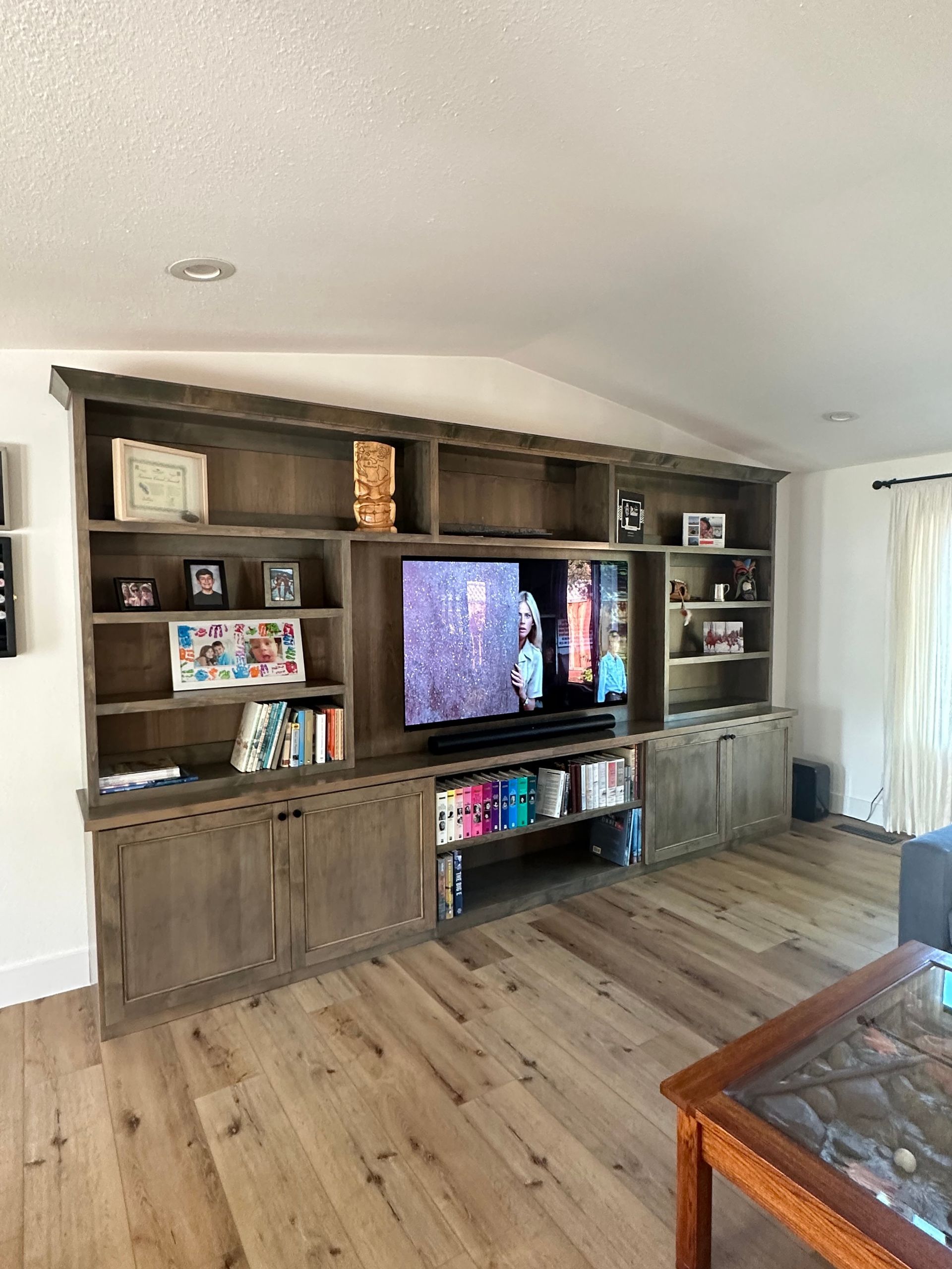 Large wooden built-in shelving unit with a central television, cabinets, and decorative items in a living room.