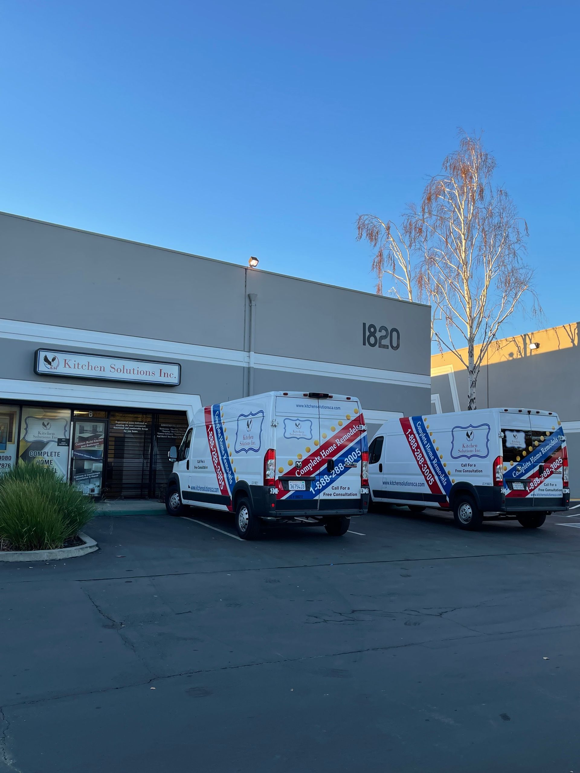 Two white service vans with blue and red stripes parked outside a gray commercial building numbered 1820.