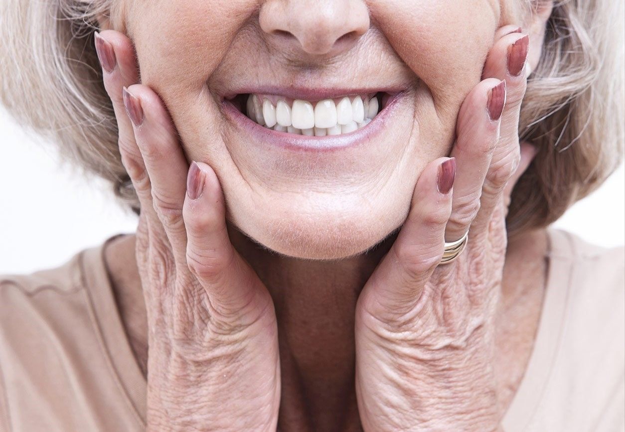 An Elderly Woman is Smiling With Her Hands on Her Face — Bytes of Byron–Bio Holistic Dentistry in Byron Bay, NSW