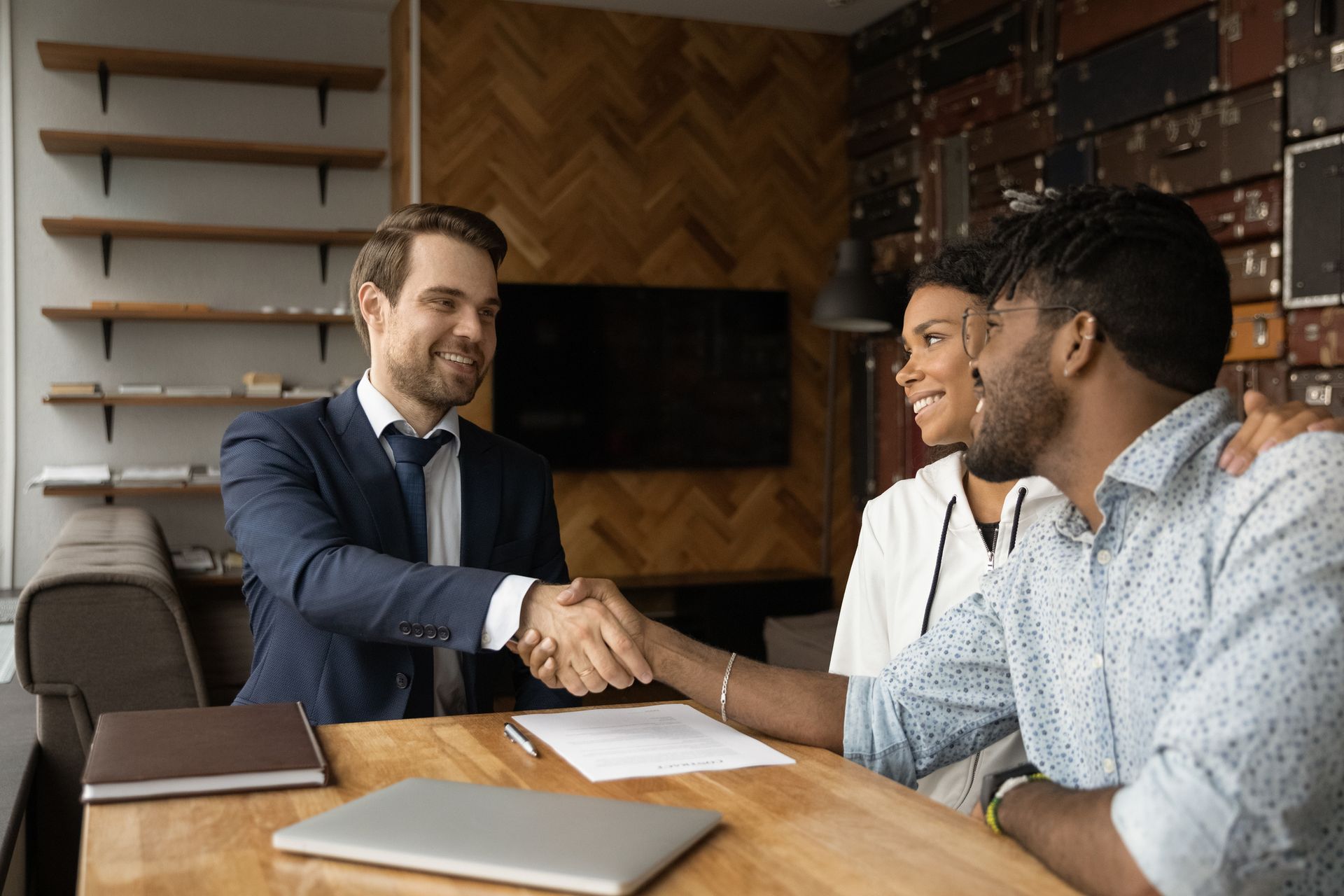 A man and woman are shaking hands with a real estate agent while sitting at a table.