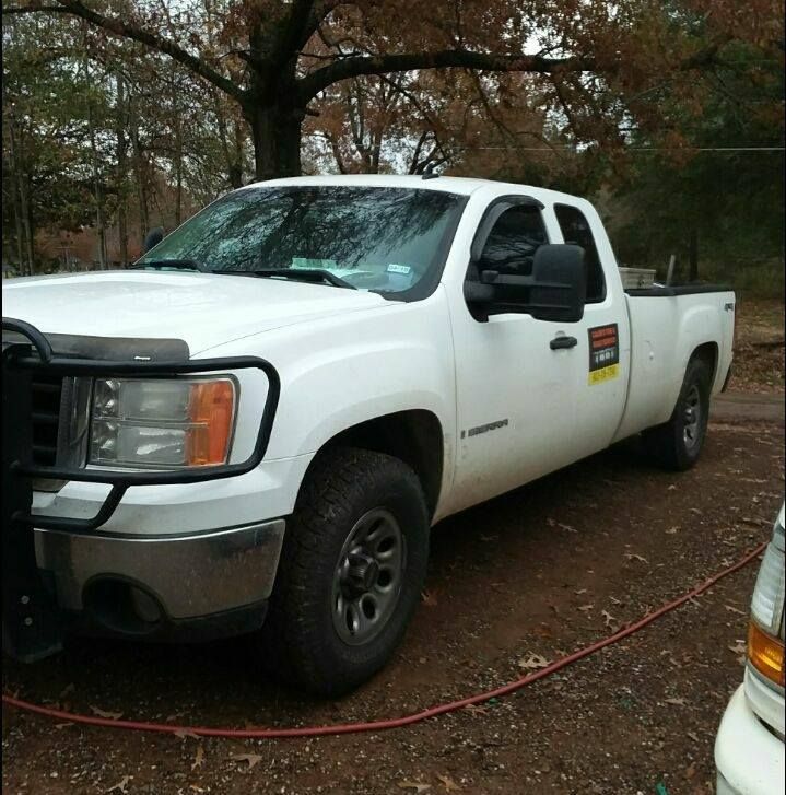 A white truck is parked in the dirt with a hose attached to it