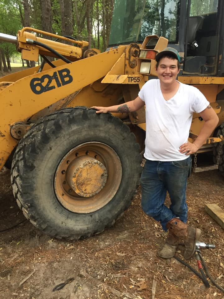 A man in a white shirt is standing next to a bulldozer.