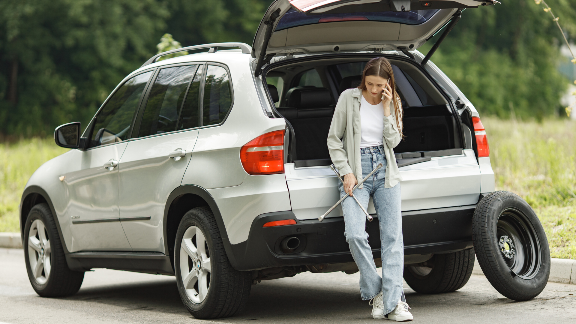 A woman is standing next to a broken down car talking on a cell phone.