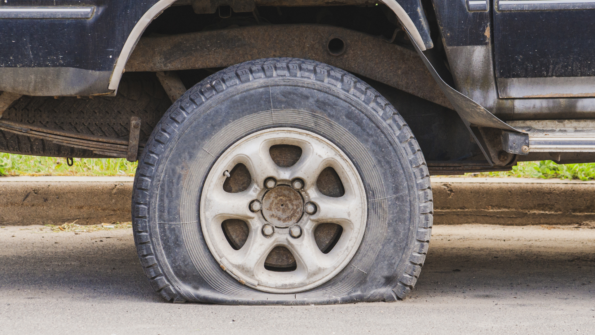 A car with a flat tire is parked on the side of the road.