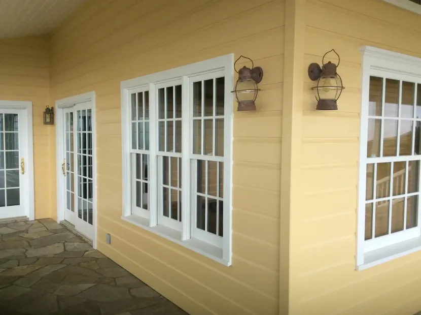 Modern living room with green sofa, fireplace, large wall TV, and wooden chairs near bright windows.