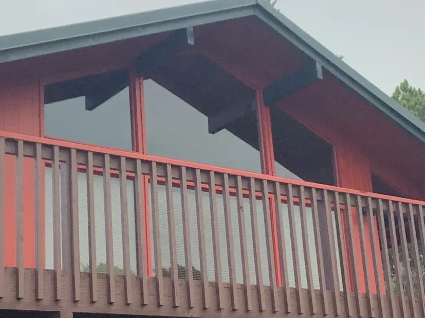 Red wooden cabin balcony with railing and large windows under a sloped roof